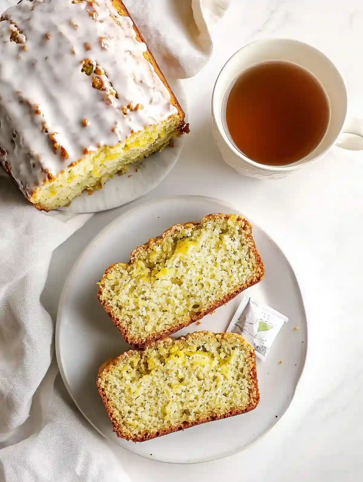Sliced gluten-free lemon zucchini bread with sour cream glaze on marble.