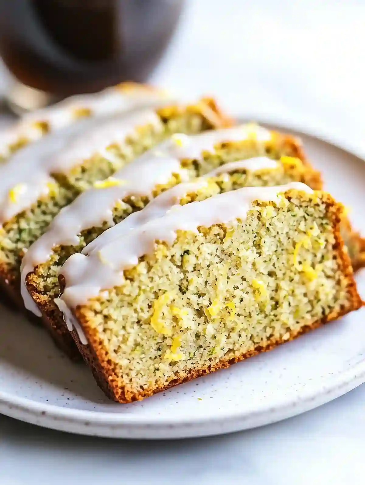 Three slices of gluten-free lemon zucchini bread with lemon glaze on a plate.