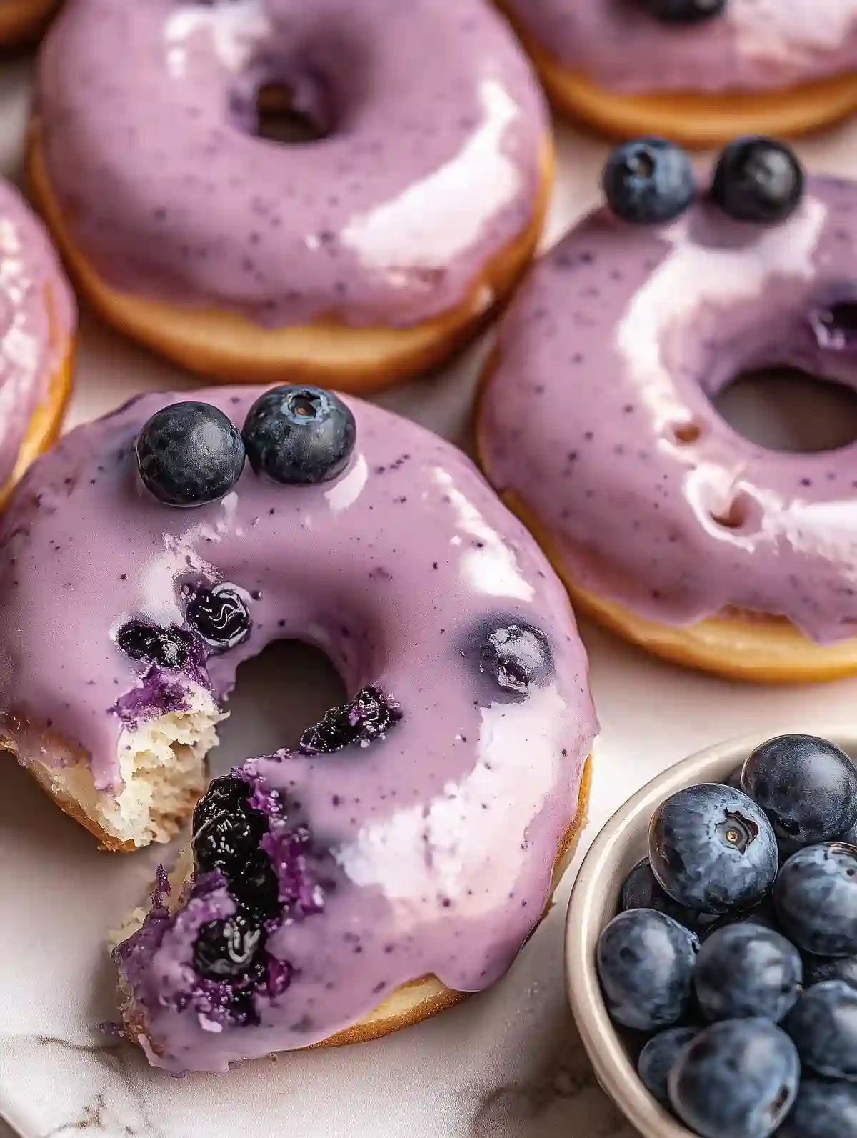 Donuts with violet glaze, blueberries, flower, on marble surface