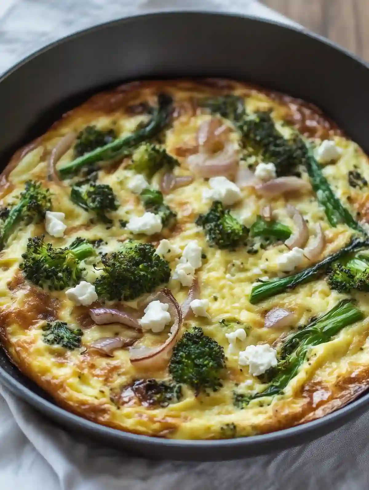 Broccolini frittata in skillet, topped with feta and sautéed onion.