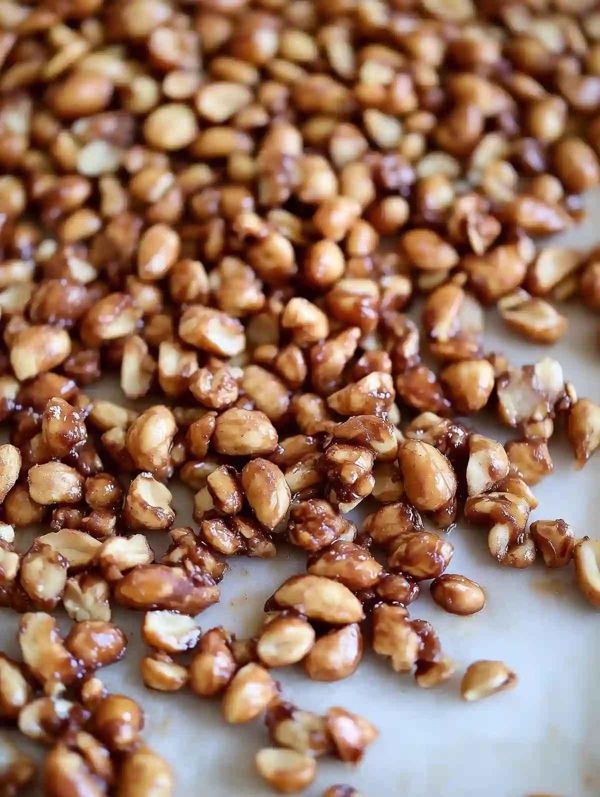 Glossy toffee-coated peanuts on white marble surface, clustered and golden