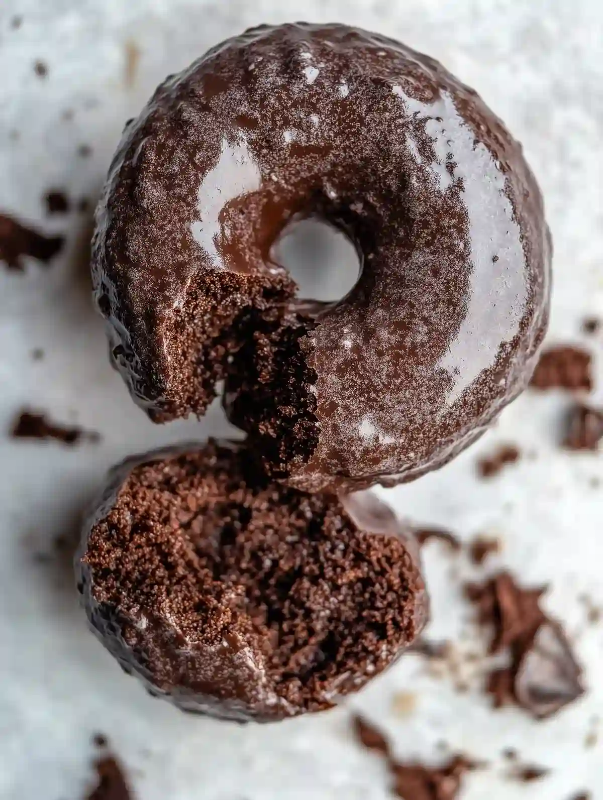 Chocolate glazed doughnut with a bite, crumbles on marble surface