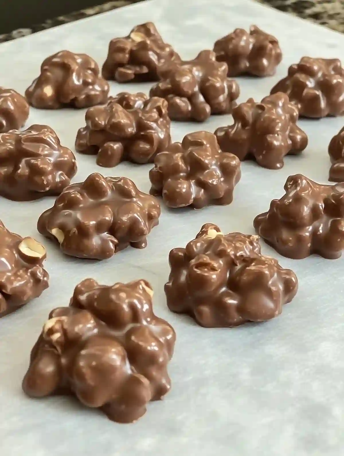 Small dark chocolate peanut clusters on white marble surface