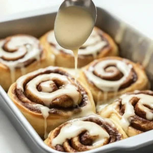 Cinnamon rolls in a baking pan, drizzled with creamy icing.