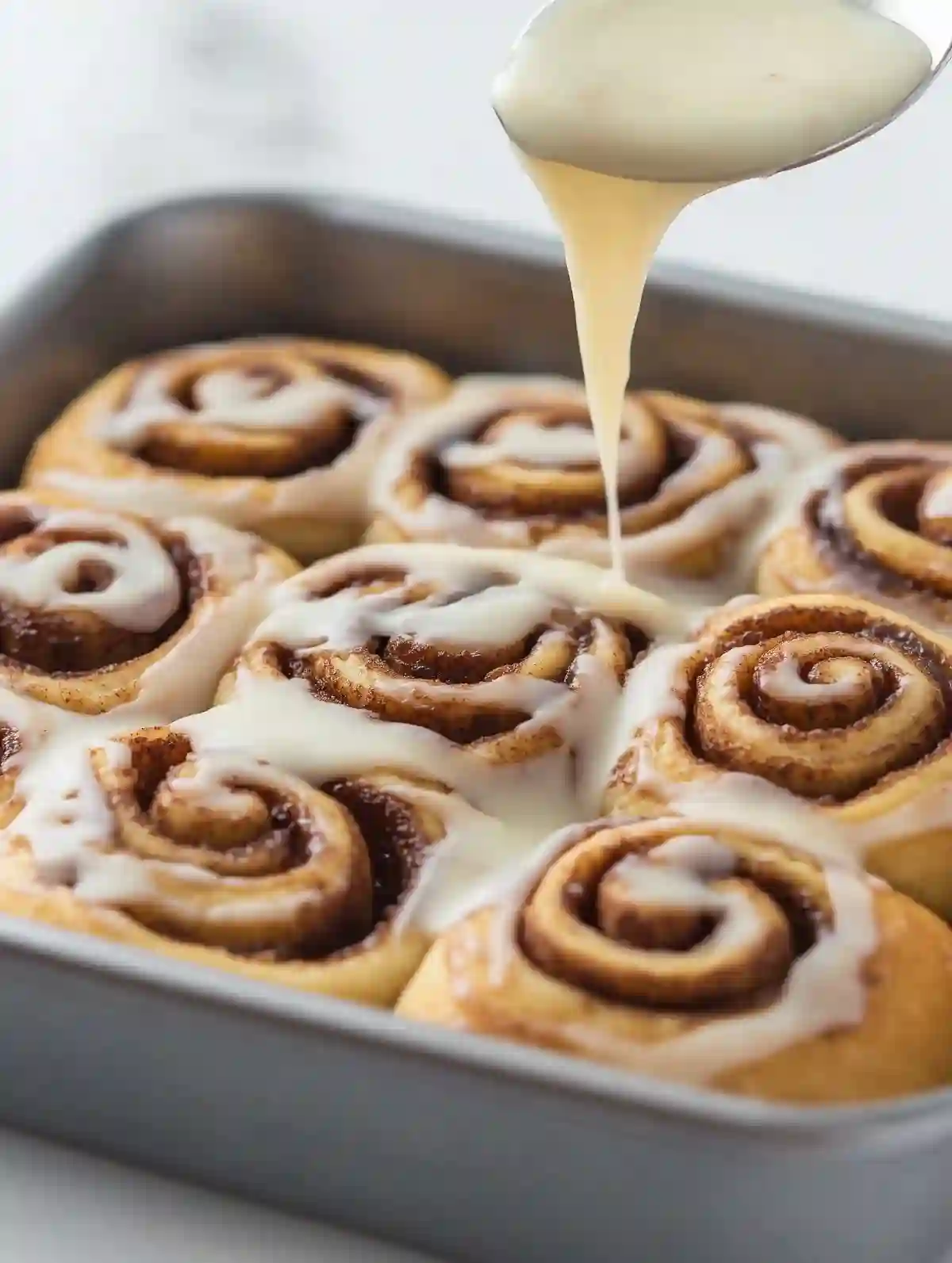 Cinnamon rolls in a baking pan, drizzled with creamy icing.
