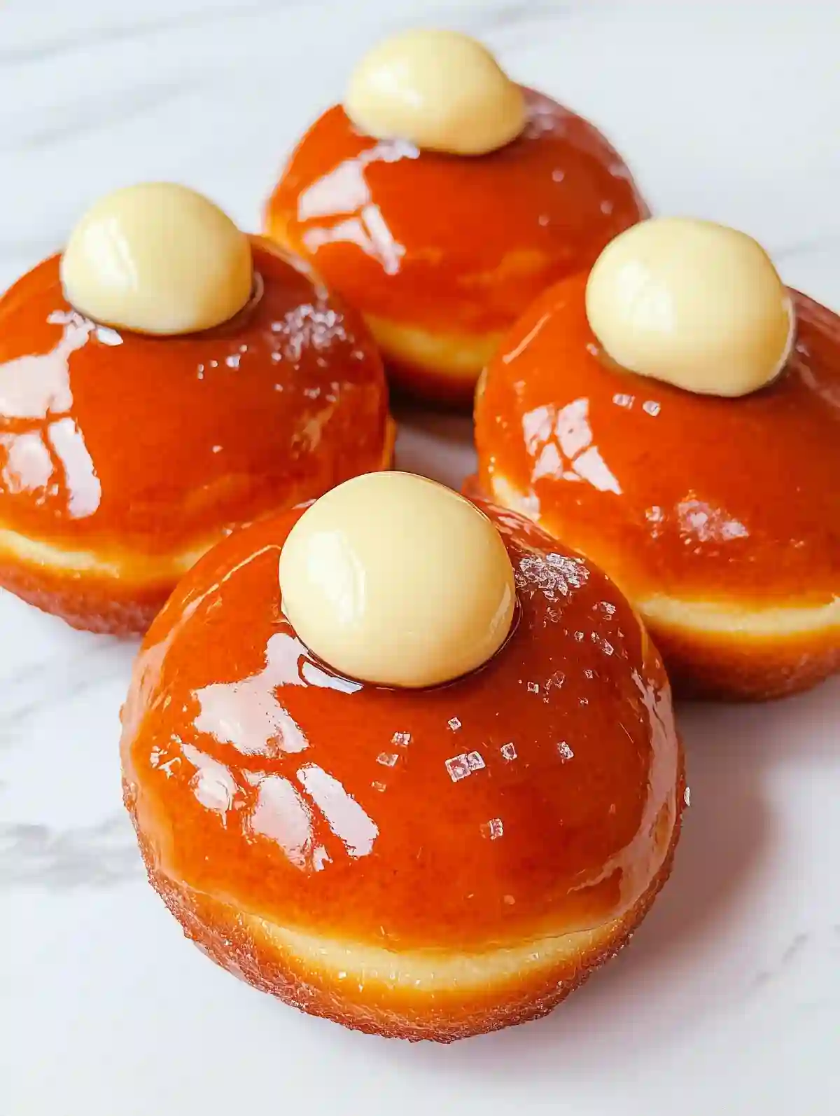 Four glazed creme brulee donuts with custard dollops on marble surface