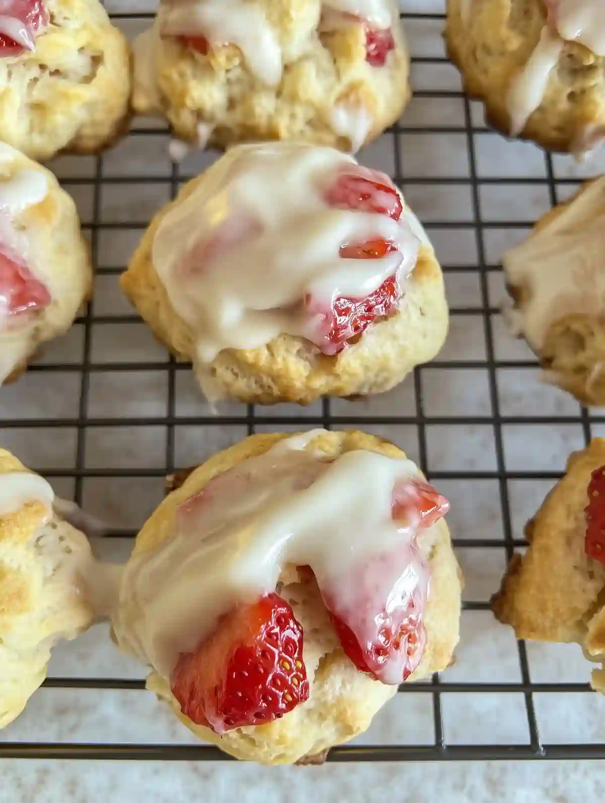 Strawberry biscuits with a white glaze on a wire cooling rack.