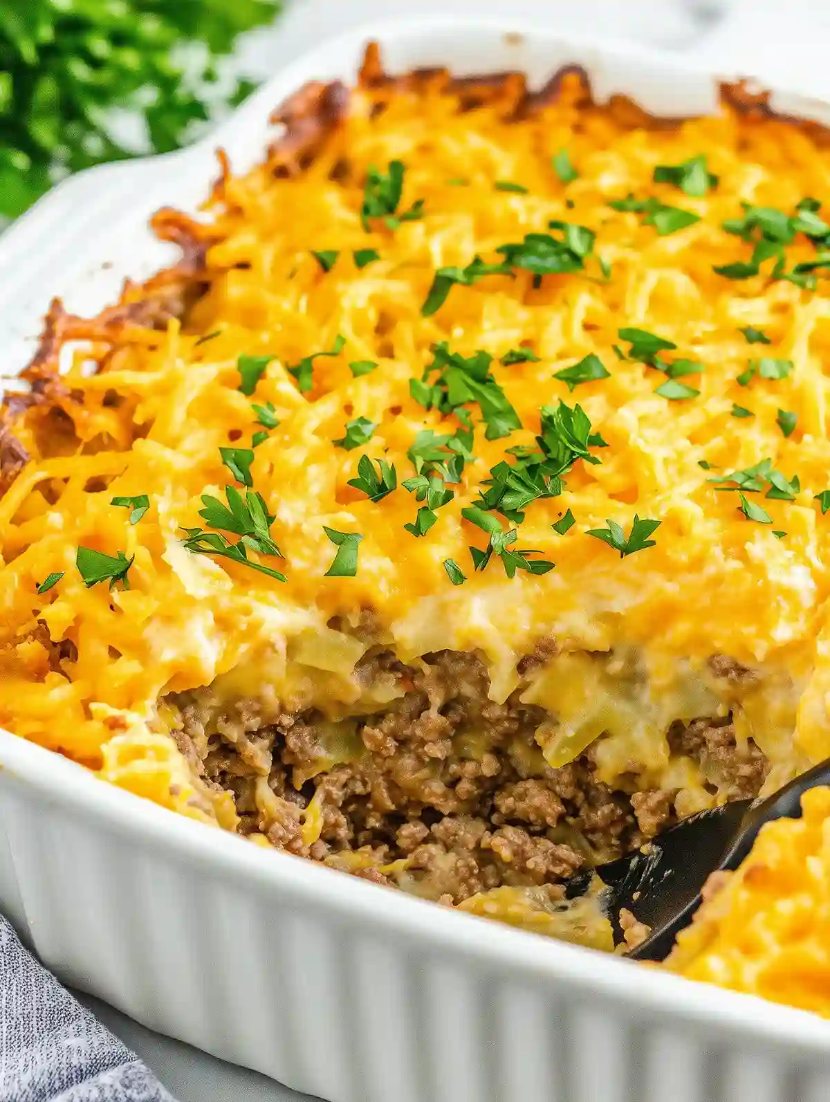 Ground beef hash brown casserole with melted cheddar, parsley garnish