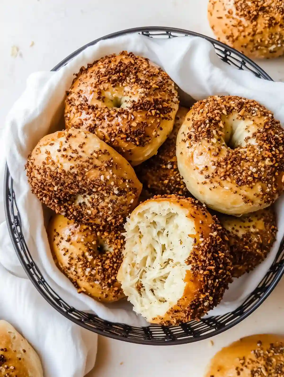 Wire basket of homemade bagels with fried onion crumbs on marble surface.