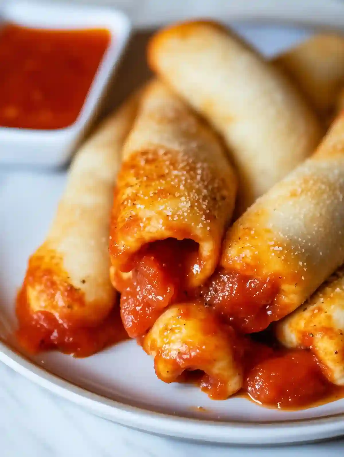 Golden-brown pizza sticks on marble surface with marinara sauce for dipping.