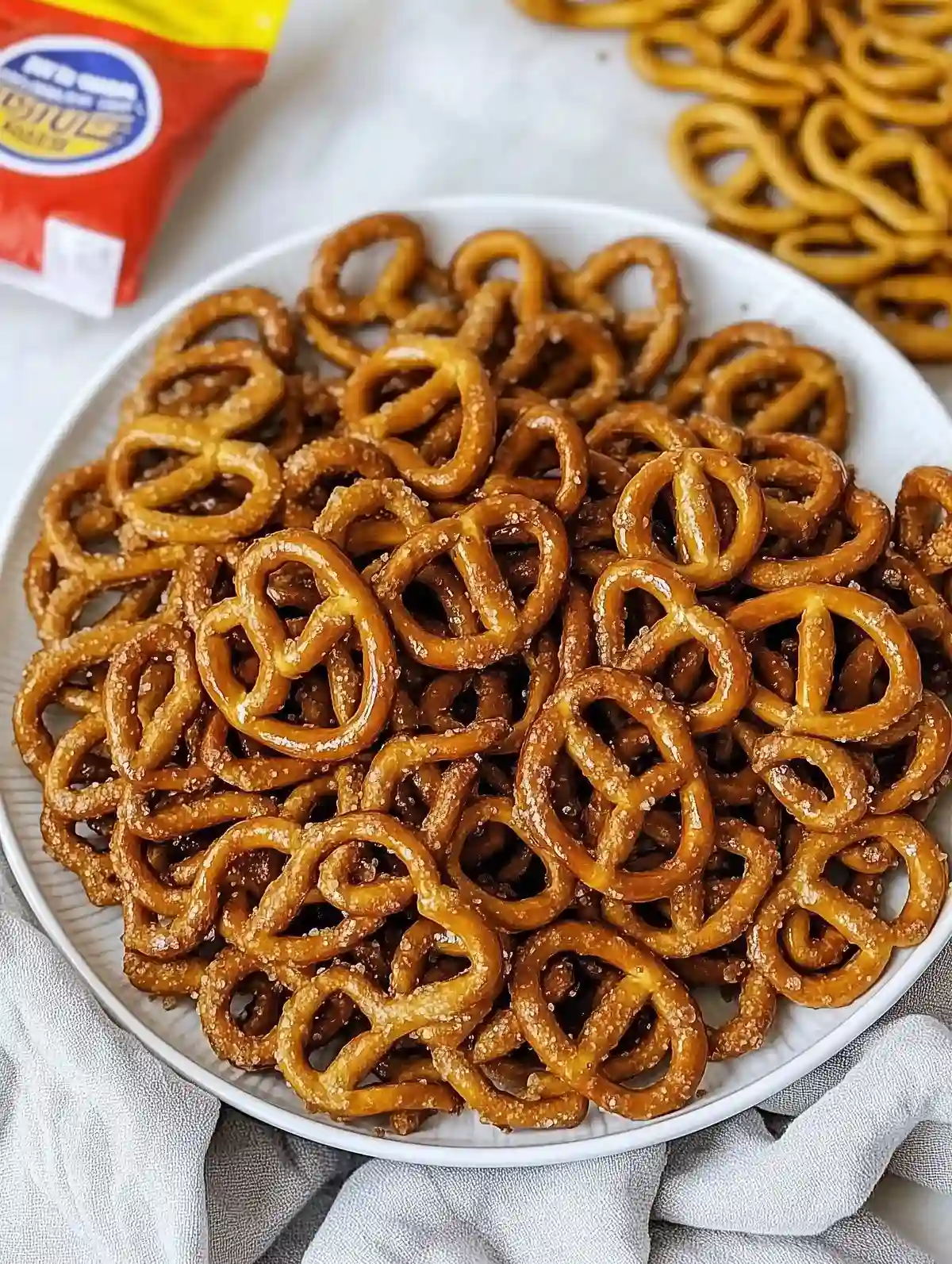 Round white plate heaped with golden-brown twisted pretzels on marble.