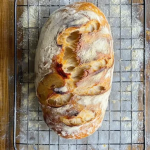 Freshly baked batard loaf on a wire rack, dusted with flour.