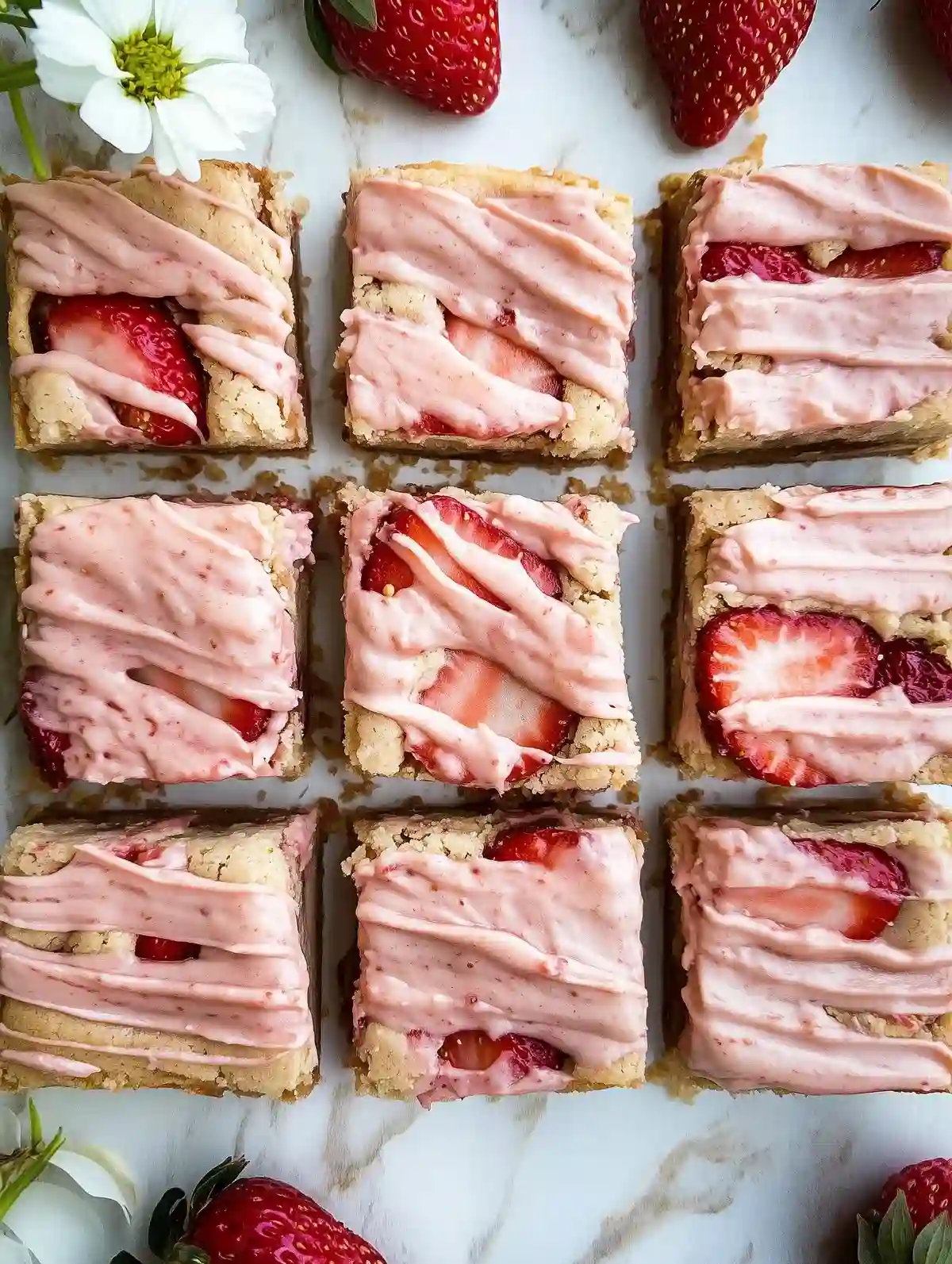 Fresh strawberry blondies with pink frosting and scattered strawberries on marble