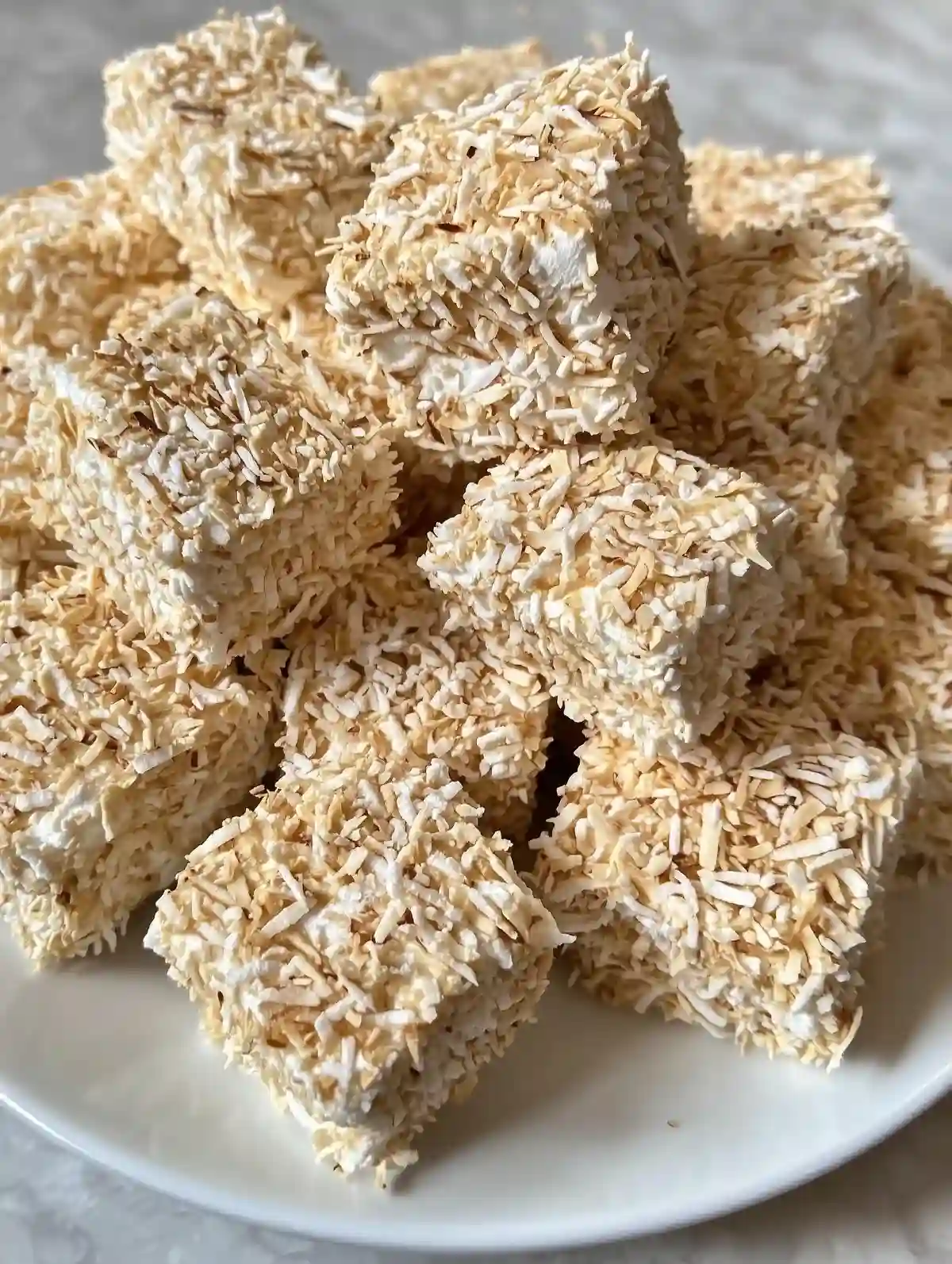 Toasted coconut marshmallows on a white plate with a marble surface