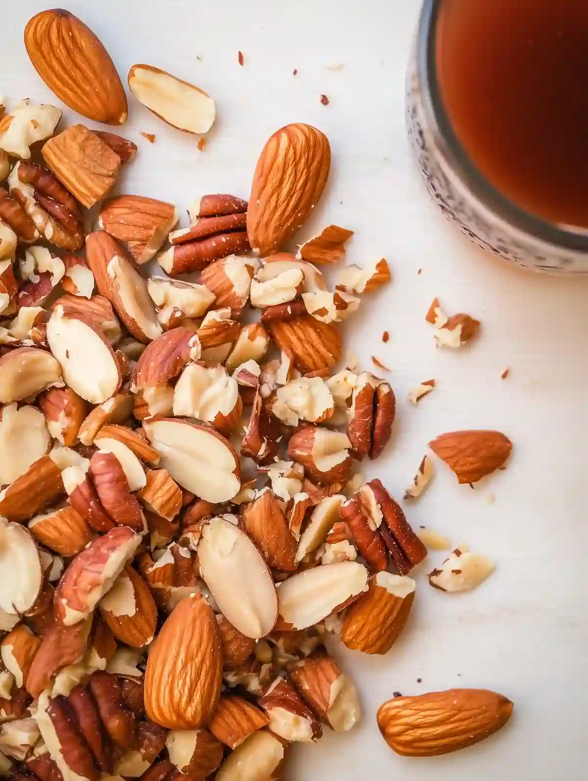 Chopped almonds and pecans on marble with a glass of dark liquid nearby