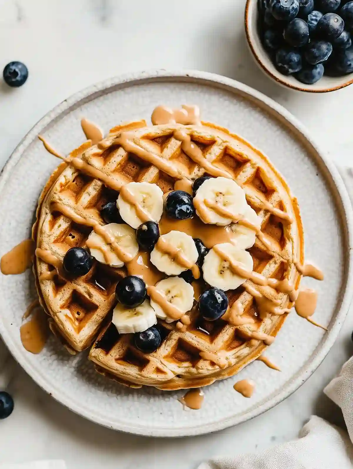 Golden-brown waffle with bananas, blueberries, and peanut butter sauce on marble