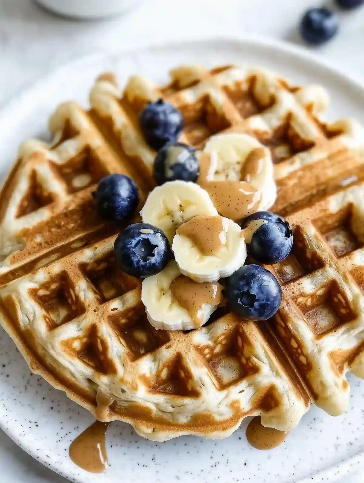Golden-brown peanut butter waffles topped with bananas and blueberries on marble