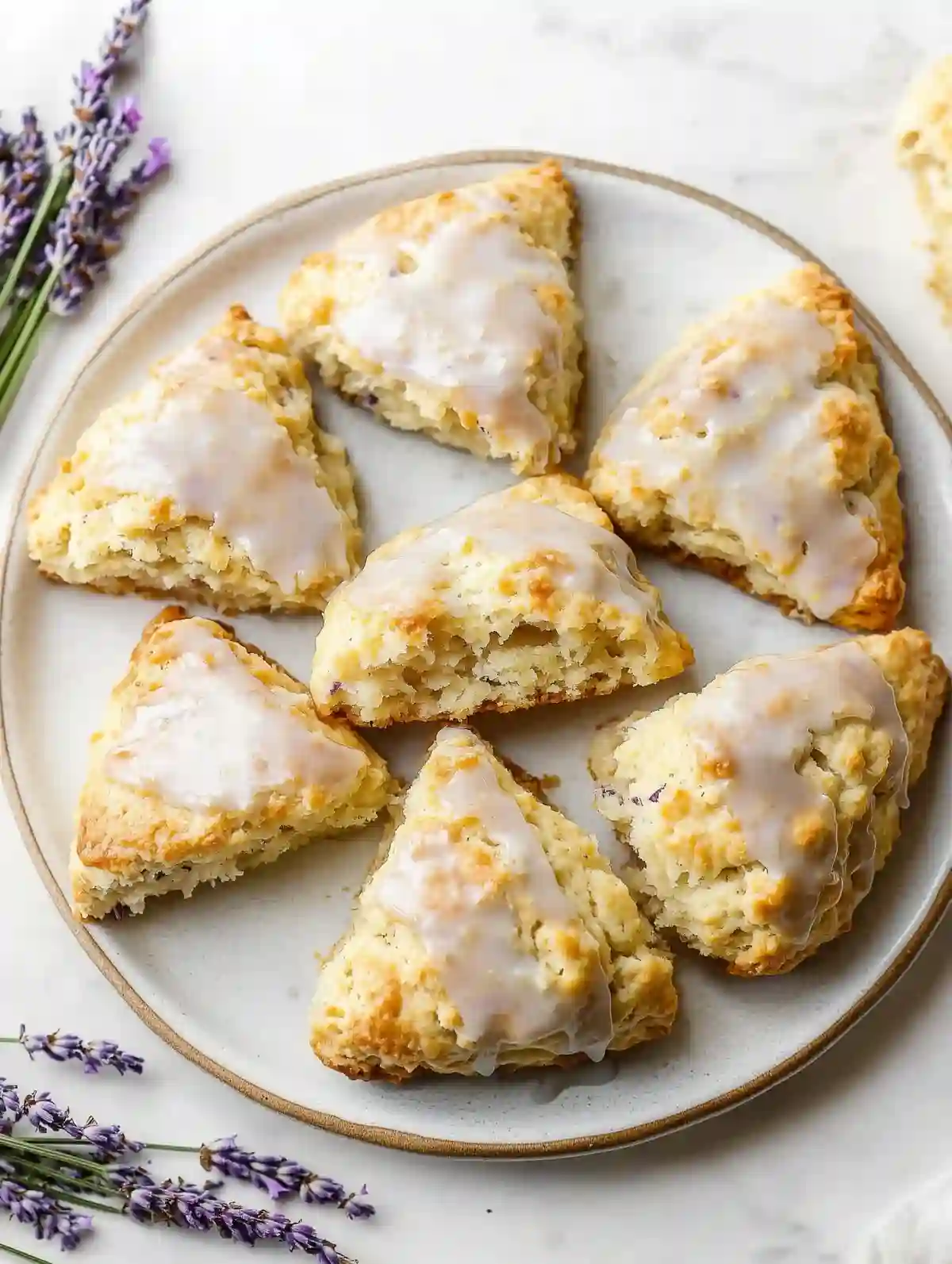 Golden-brown lemon lavender scones with glaze on a white plate, garnished with dried lavender.
