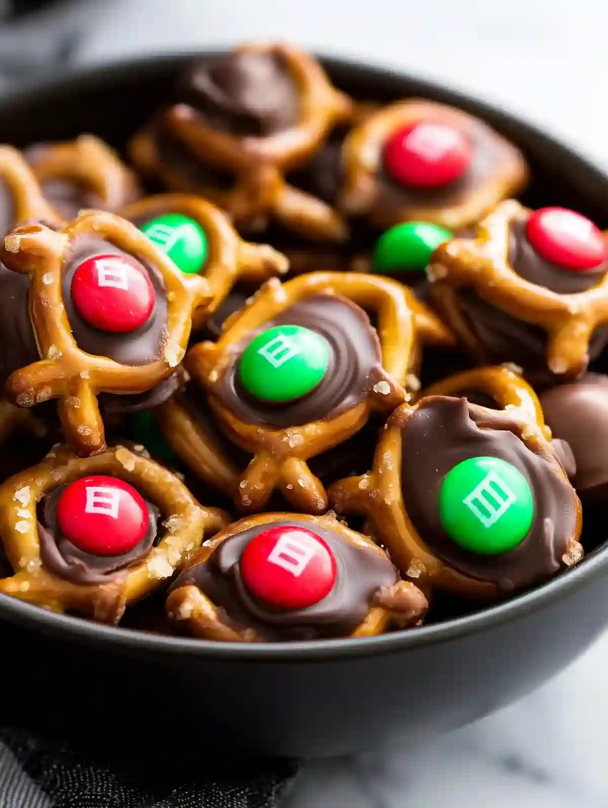 Black bowl with pretzel Rolo M&M bites on white marble surface