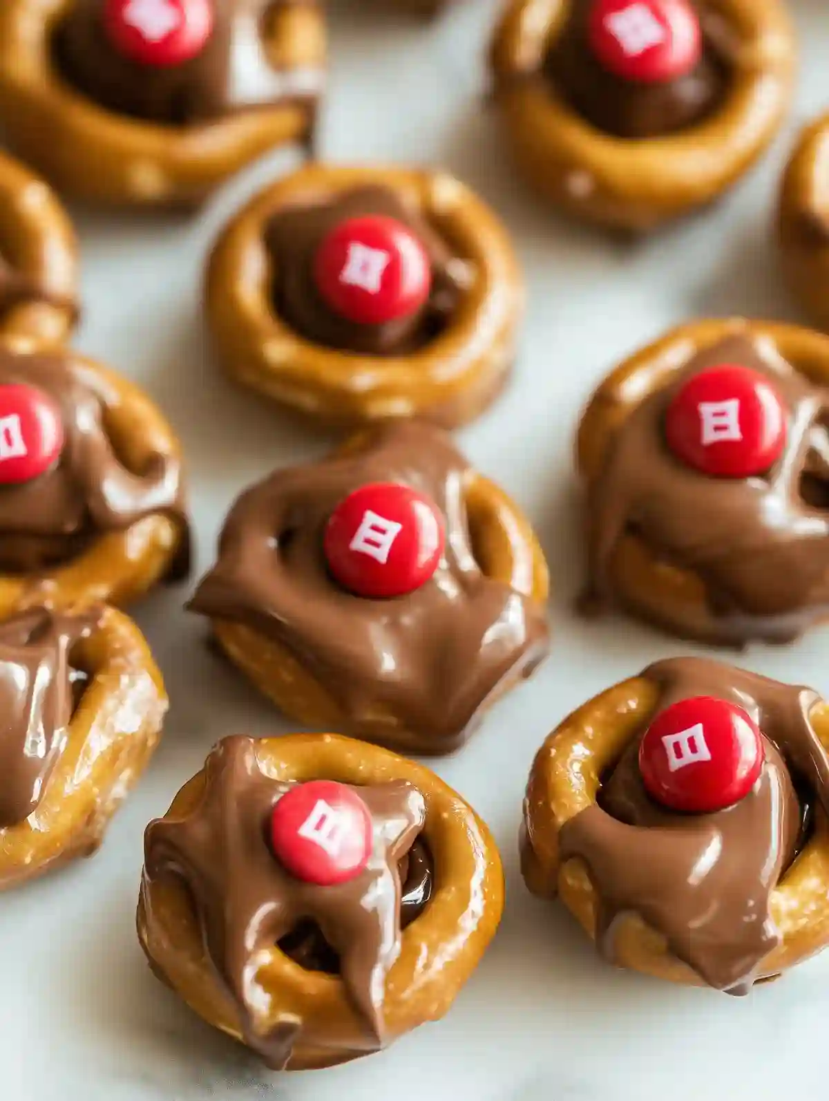 Mini pretzels topped with melted chocolate and red M&Ms on marble surface