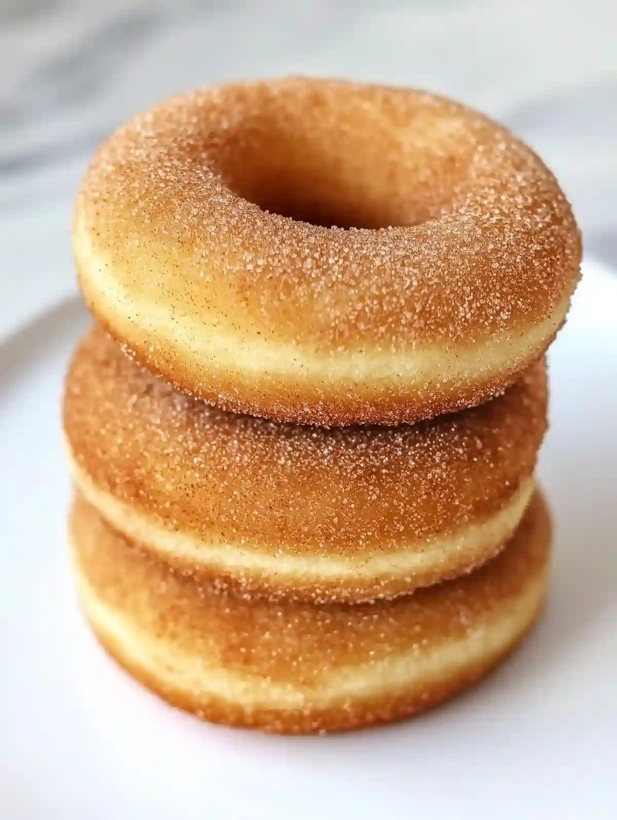 Stacked golden-brown cinnamon-sugar donuts on a white marble surface