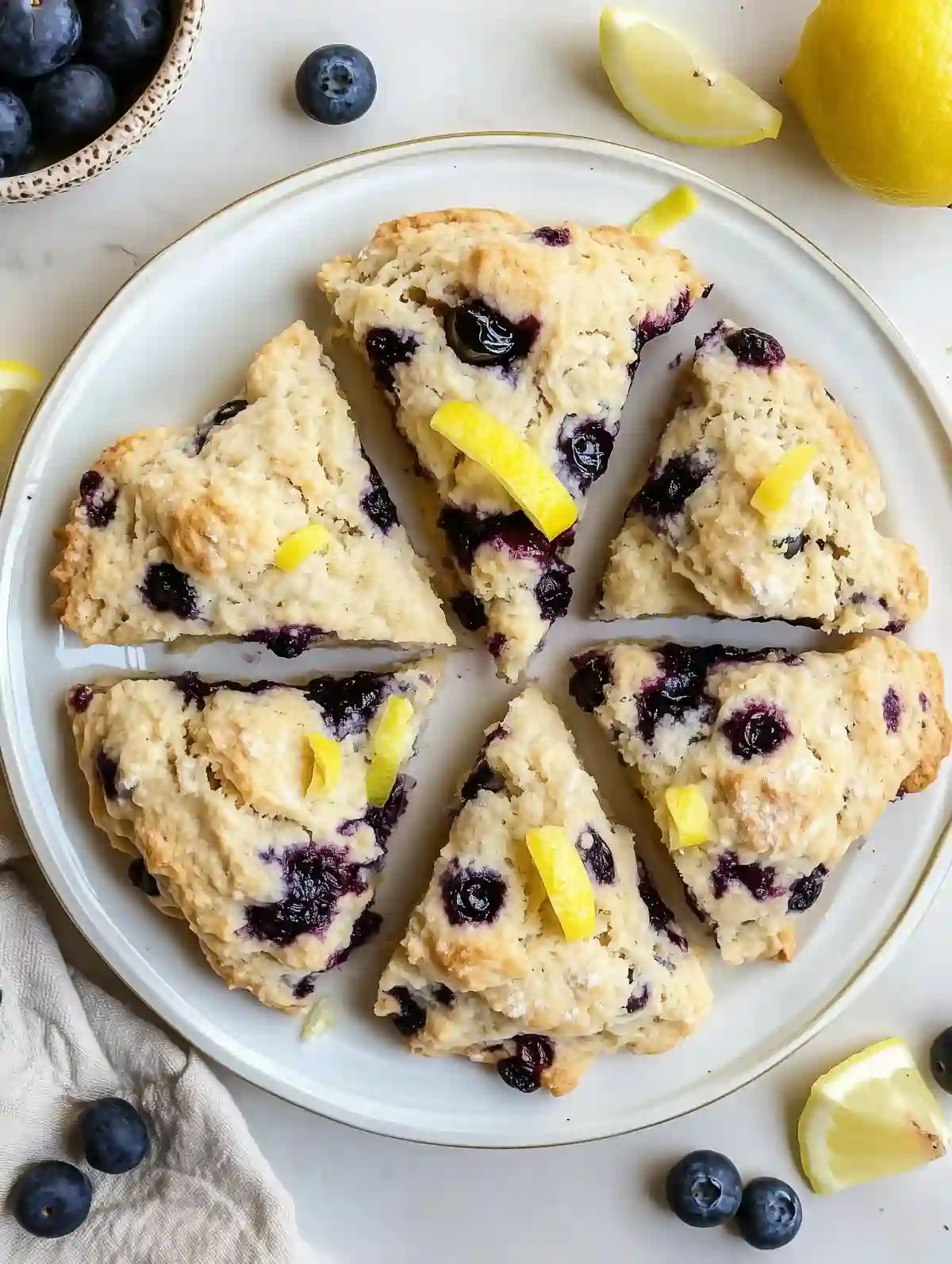Circular plate of golden-brown blueberry scones with lemon zest and fresh blueberries.