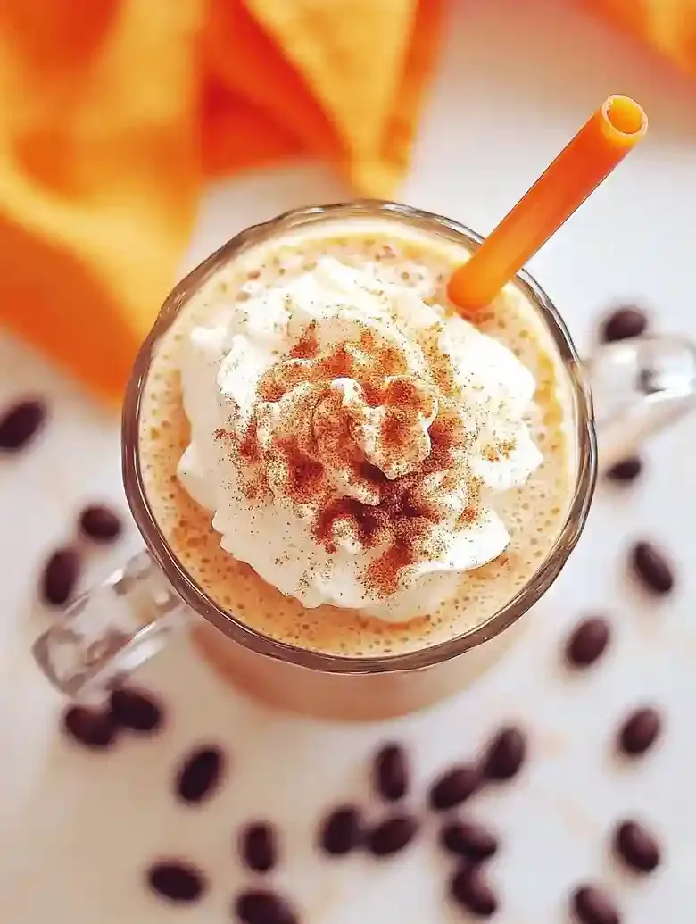 Pumpkin frappuccino with whipped cream and cinnamon on marble surface.