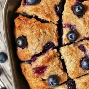 Golden-brown square blueberry biscuits in a baking dish on marble surface.