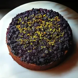 Blueberry upside-down cake with lemon zest on a white marble surface.