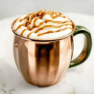 Caramel Brûlée Latte in a copper mug, topped with whipped cream and toffee bits.