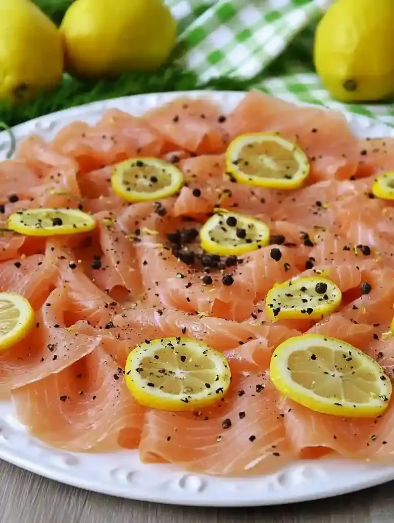 Sliced smoked salmon with lemon and pepper on a marble surface.