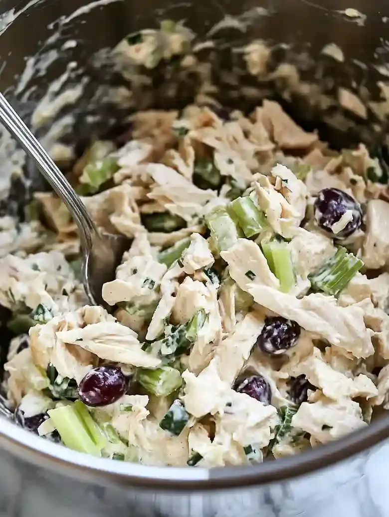 Stainless steel bowl with chicken salad, celery, grapes, and green onions.