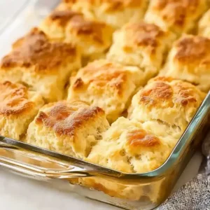 Golden-brown baked biscuits arranged in a glass dish on marble surface.