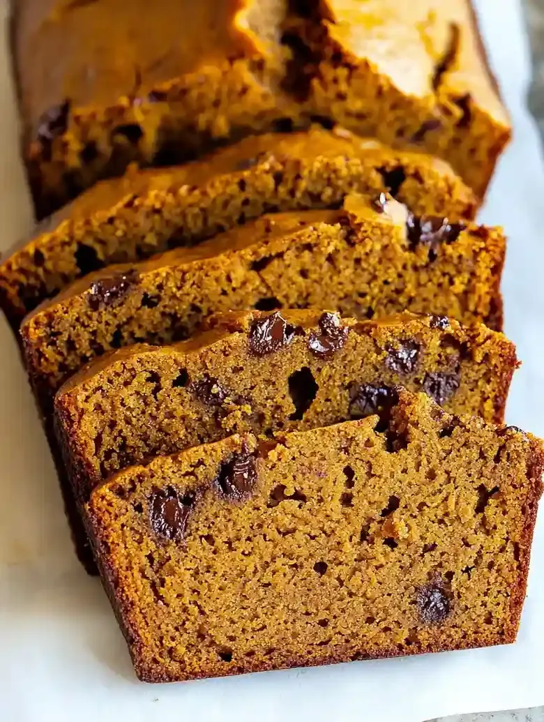 Golden-brown pumpkin loaf slices with chocolate chips on marble surface.