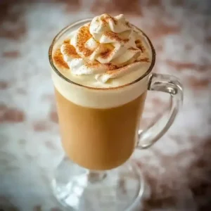 Tall glass mug with tan beverage topped with whipped cream and cinnamon.
