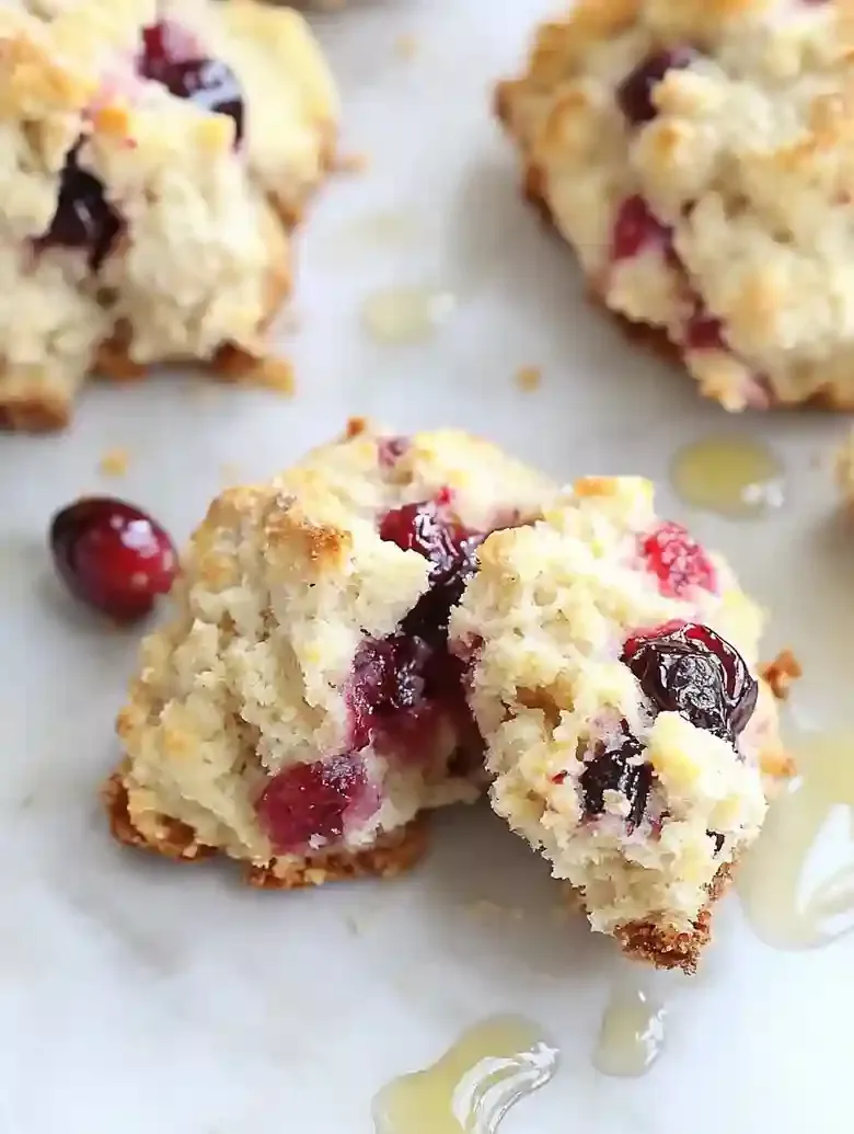 Cranberry orange biscuits on marble surface with honey drizzle.
