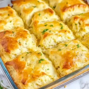 Square golden-brown biscuits with herbs in a glass baking dish on marble.