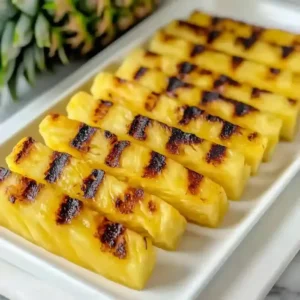 Grilled pineapple spears on a white plate, whole pineapple in background.