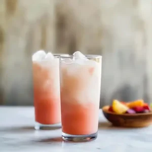 Two tall glasses of a mixed drink with ice on a marble surface.