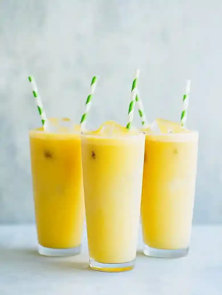 Three tall glasses of yellow beverage with frothy tops and striped straws.