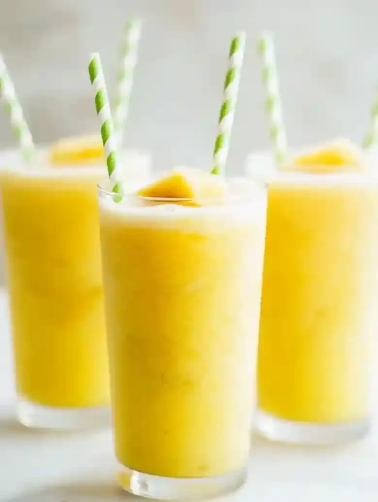 Three tall glasses of yellow iced drinks with frothy tops and striped straws.