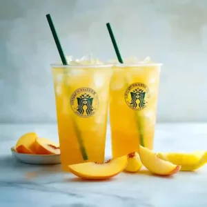 Two tall cups with yellow iced beverage, peach slices, and lemon wedges.