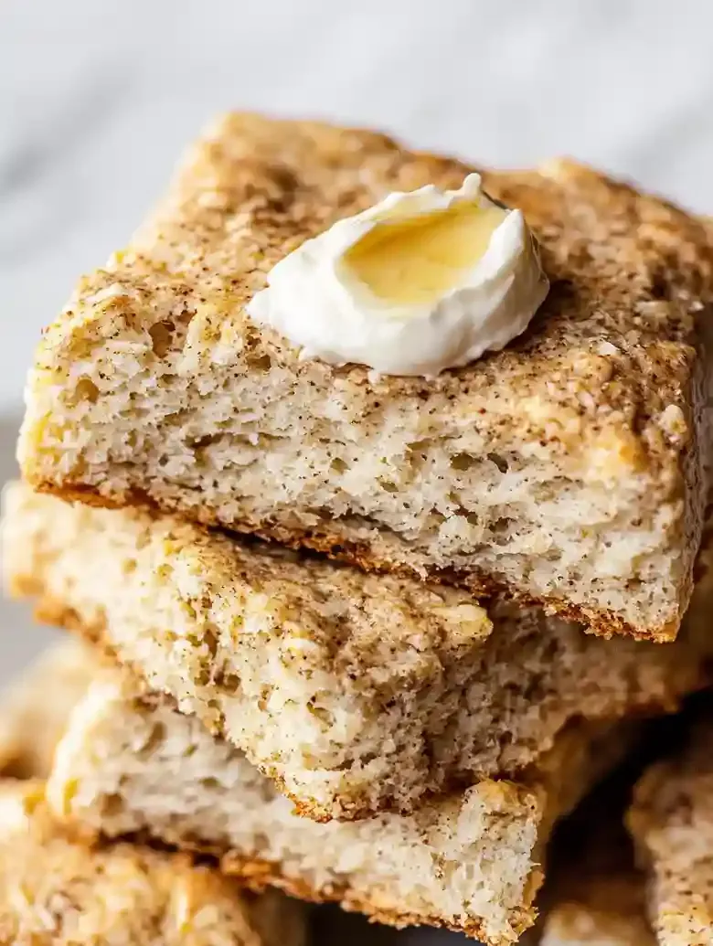 Stack of golden-brown maple pecan biscuits with syrup on a marble surface.