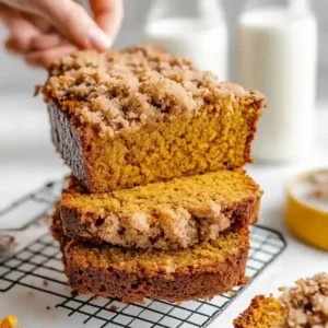 Hand reaching for a slice of pumpkin bread on a wire rack.