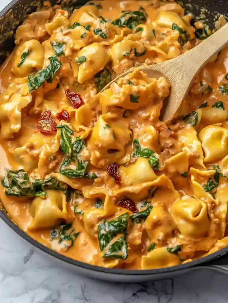 Skillet of cheese tortellini in orange sauce with spinach and sundried tomatoes.