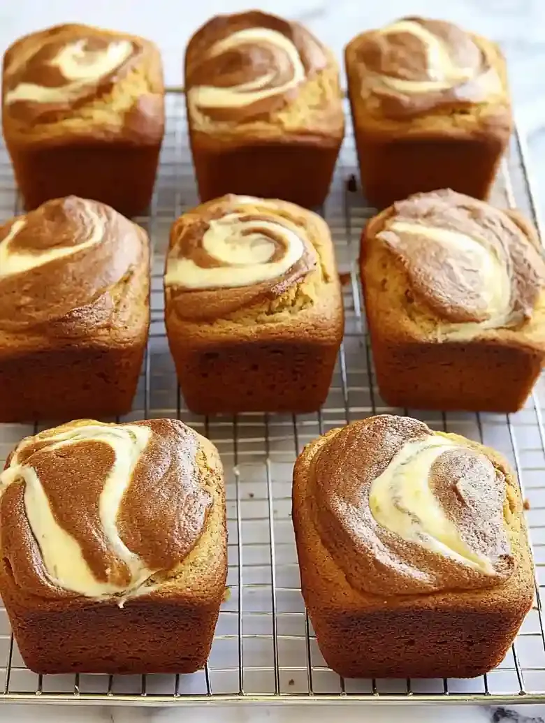 Ten mini loaves of pumpkin cream cheese bread on a wire rack.