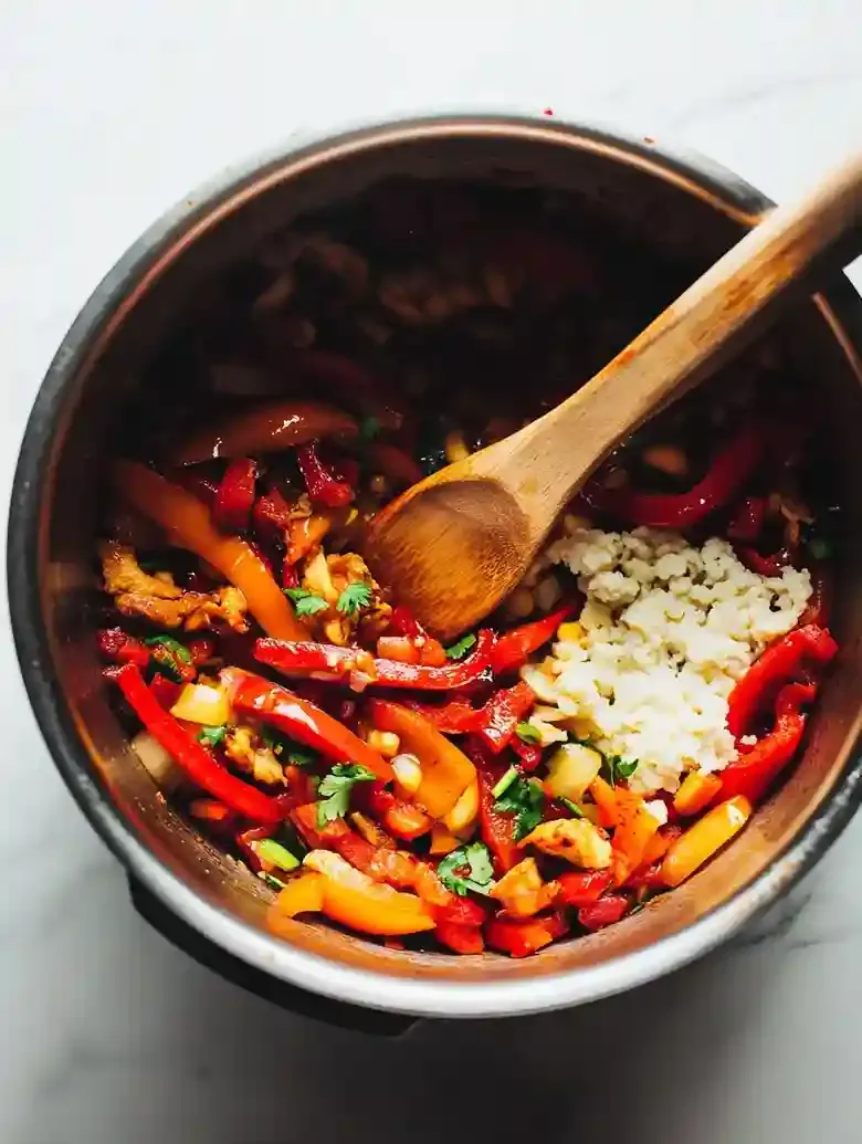 Silver pot filled with sautéed bell peppers, shallots, ginger, and garlic.