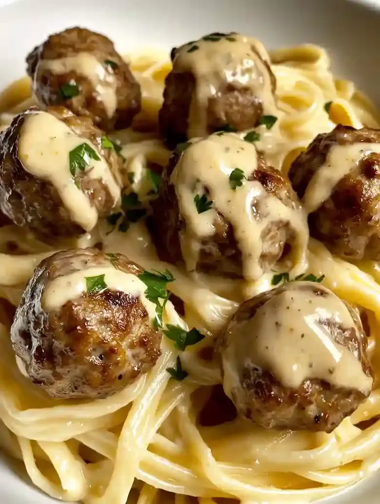 Linguine pasta topped with golden meatballs and parsley in a white bowl.