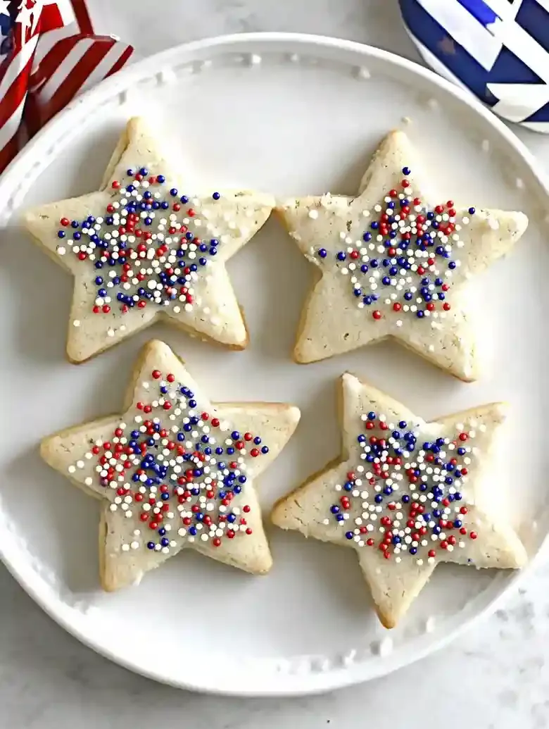 Four star-shaped cookies with red, white, and blue sprinkles on marble.