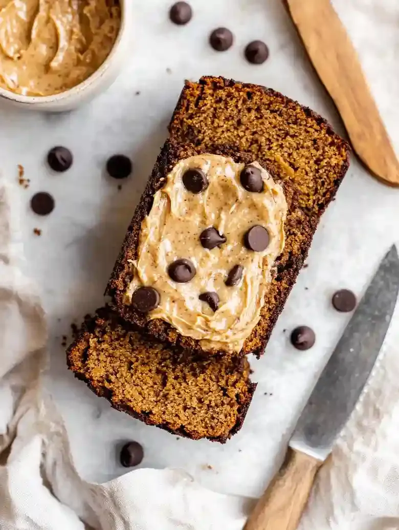 Three slices of pumpkin loaf with chocolate chips and nut butter on marble.